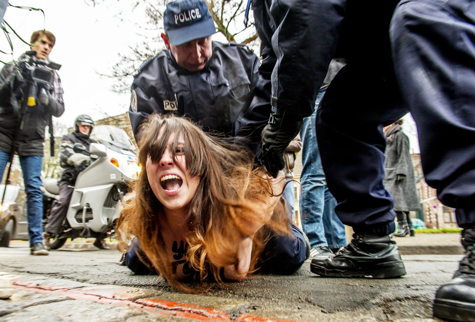 Policemen detain a topless Femen activist after she jumped in front of the car carrying former IMF chief Dominique Strauss-Kahn (not seen) upon his arrival for his trial in Lille, northern France, on February 10, 2015. Three topless women from the protest group Femen jumped on the car of Dominique Strauss-Kahn as the former IMF chief arrived to testify at his trial for "aggravated pimping." With slogans scrawled on their half-naked bodies and hurling insults at the car, the three protesters were quickly rounded up by police as the car entered an underground parking area. AFP PHOTO / PHILIPPE HUGUEN (Photo credit should read PHILIPPE HUGUEN/AFP/Getty Images)